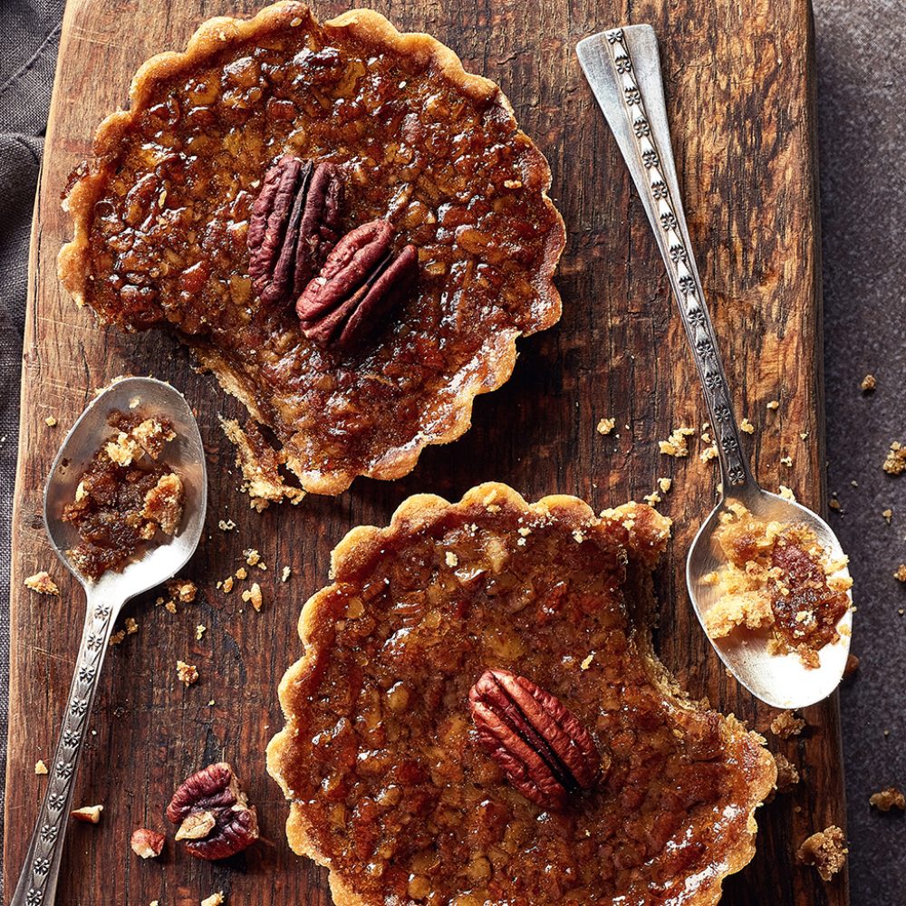 Homemade mapple syrup and pecan tarts on wooden cutting board from top view